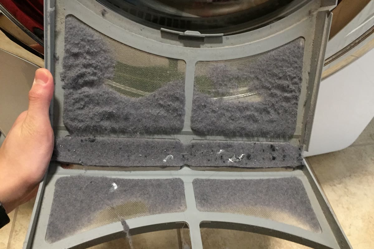 A lint-covered dryer screen held in front of an open clothes dryer.